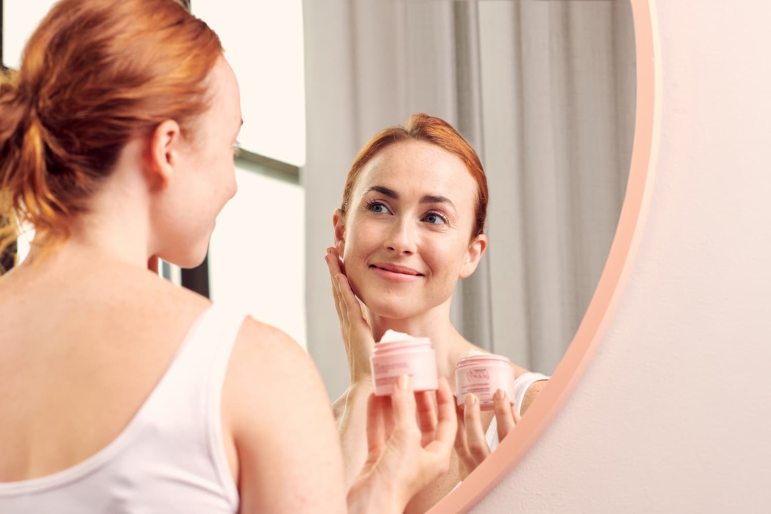 Woman gleefully applying face cream in mirror