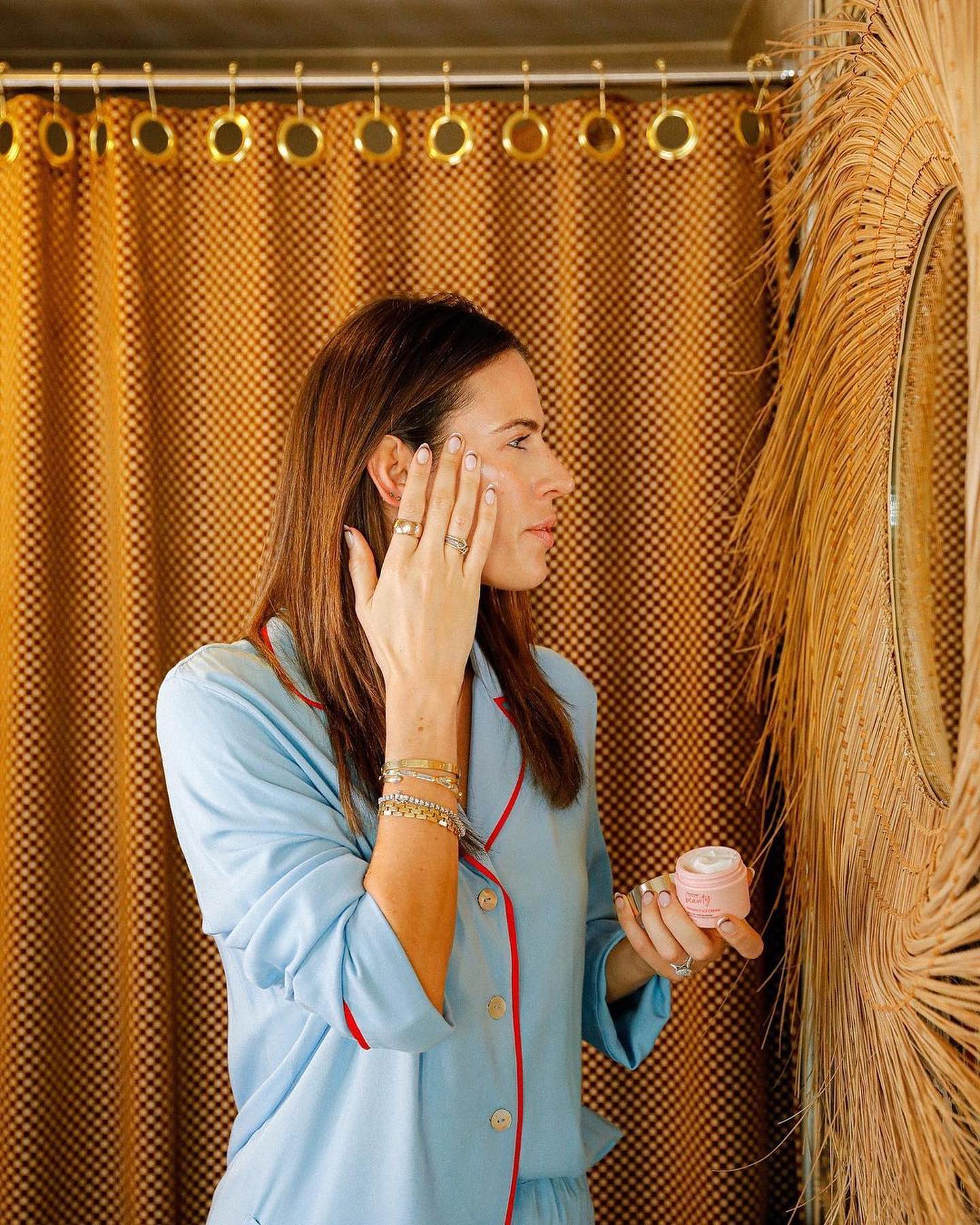 Woman applying cream in mirror, photo taken from side