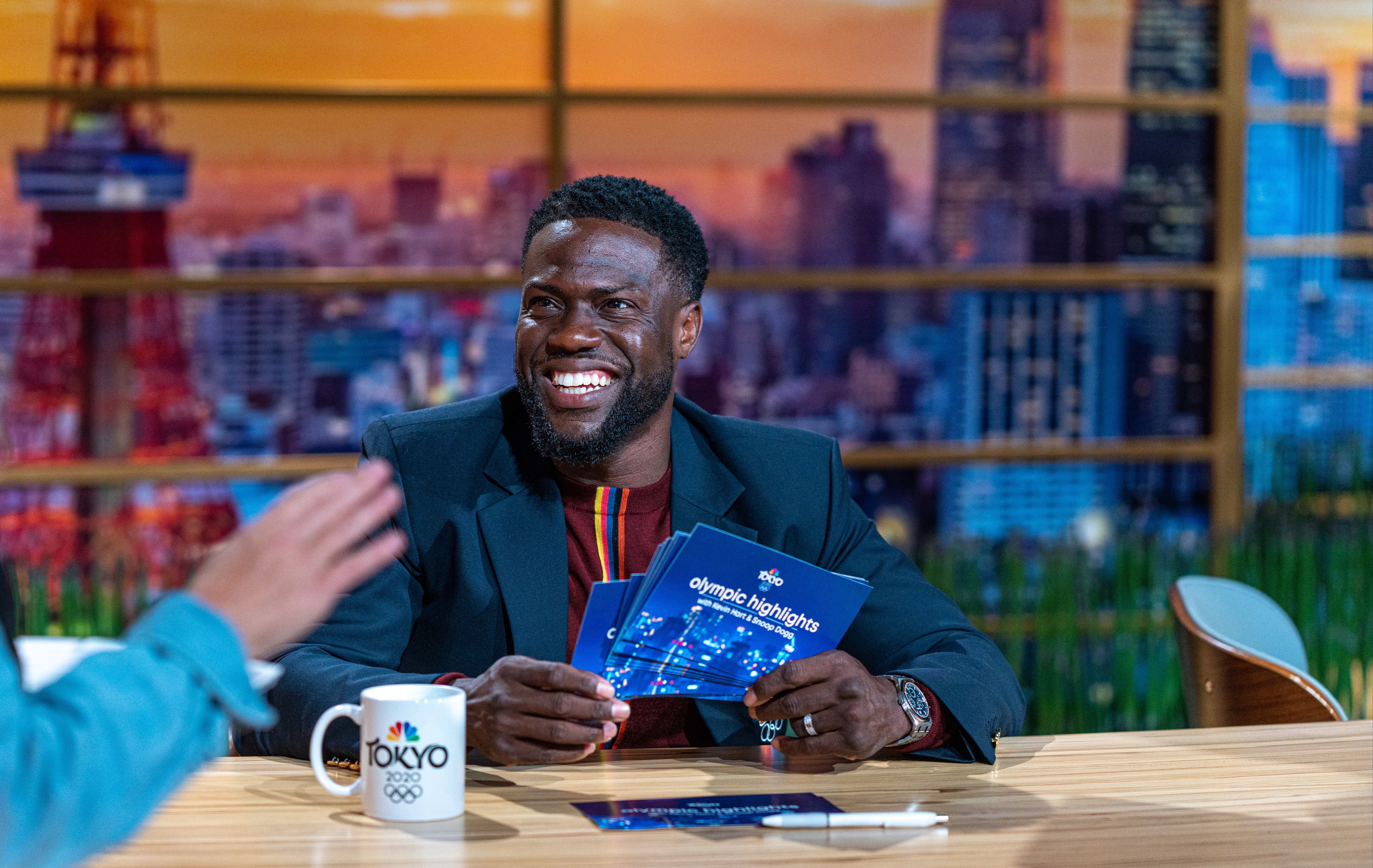 Kevin Hart sitting at news desk smiling