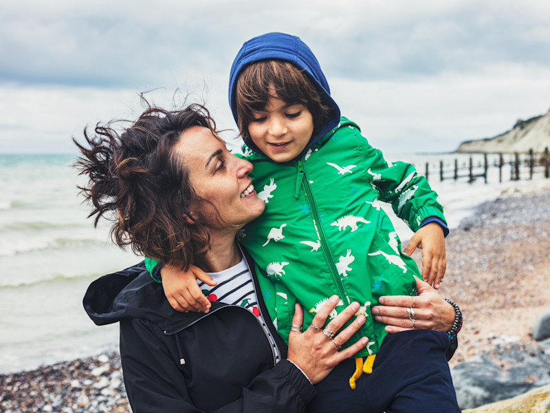 A smiling mother holding a child on a windy beach.