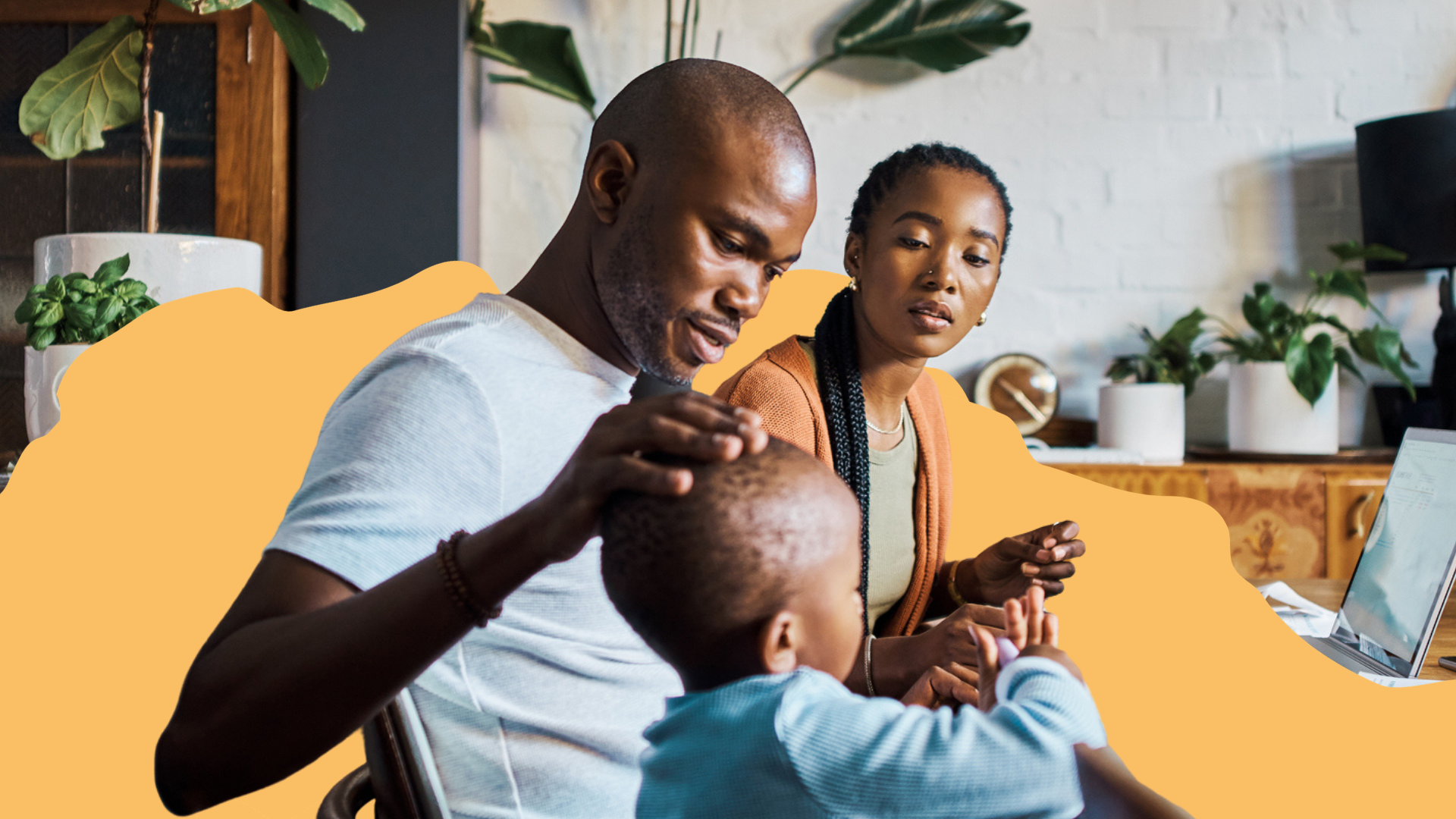 A family made up of a father, mother and child sit at a table together with a laptop in front of them.