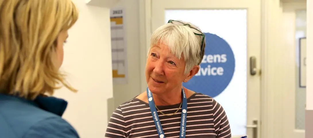 An adviser wearing a Citizens Advice lanyard talks to a blonde woman in a hallway