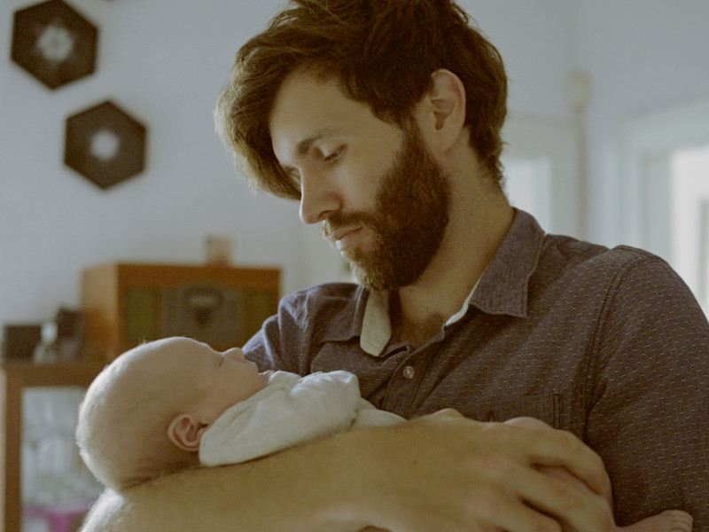 A young father is holding his baby and looking worried.