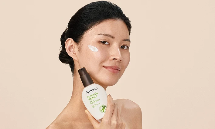 Woman with cream on her face, featuring Aveeno® Positively Radiant® Antioxidant Brightening Power