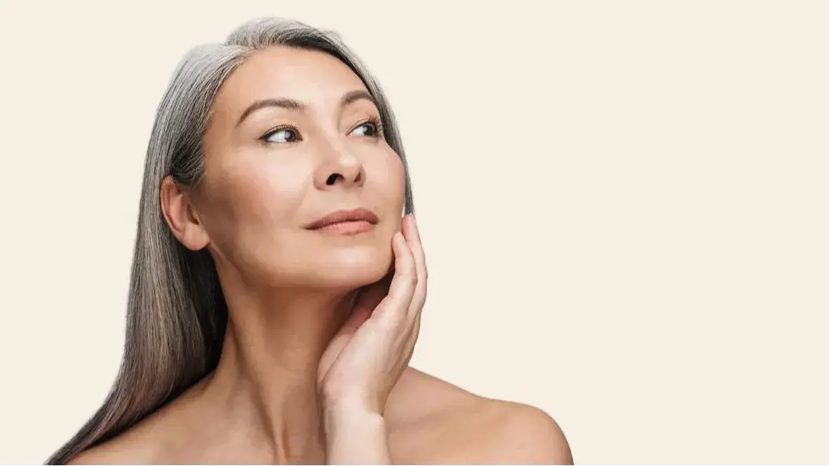 Older woman with gray hair gently touching her cheek looking to the side