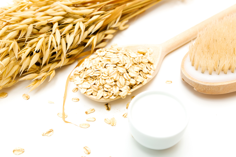 A young woman sits at a table and prepares a mask with oats for dry skin.