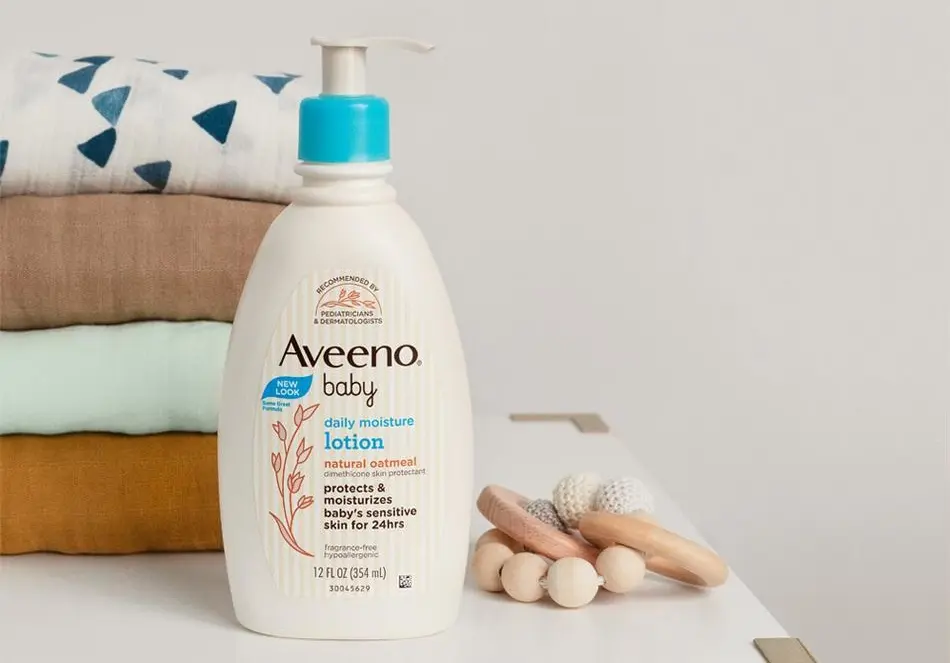 Aveeno® Baby Daily Moisture Lotion on a surface with folded baby towels and a toy