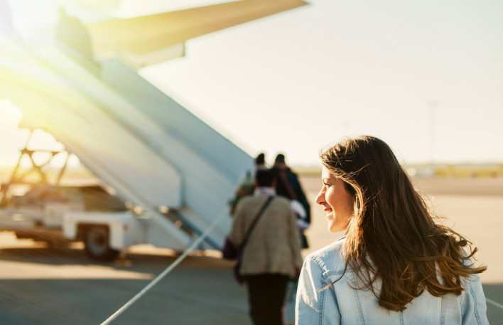 Woman tourist passager getting in to airplane at airport, walking from the terminal to the plane.