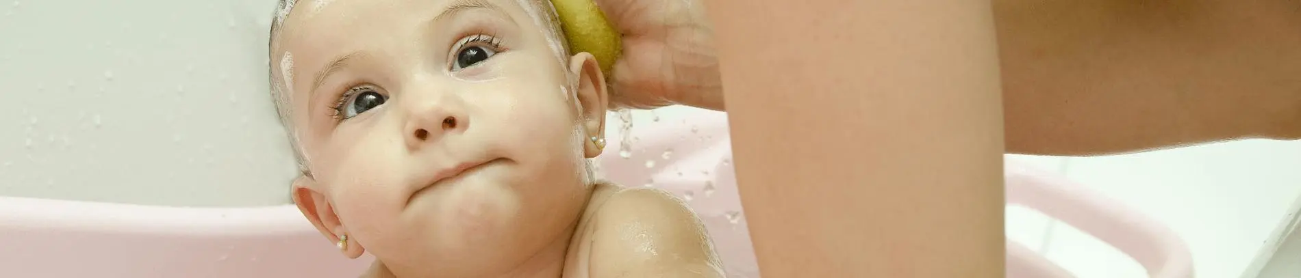 A baby getting a bath while being gently washed with a sponge in a pink bathtub.