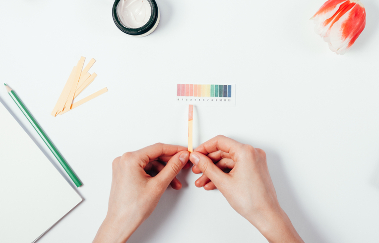 A pair of hands holds a pH strip above a white background.