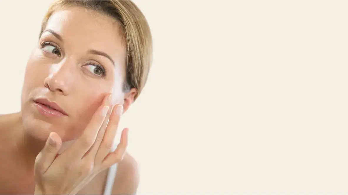 Woman looking at her reflection as she gently touches her cheek, as if she's examining her skin