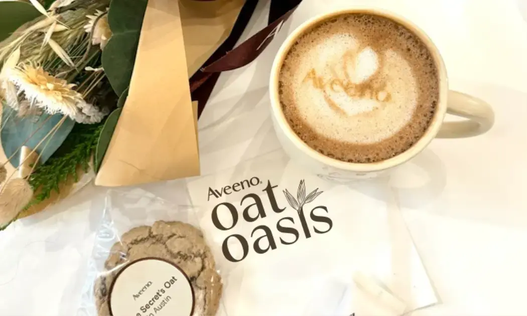 Coffee with text Aveeno® and napkin with text Aveeno® Oat Oasis surrounded by flowers and cookie