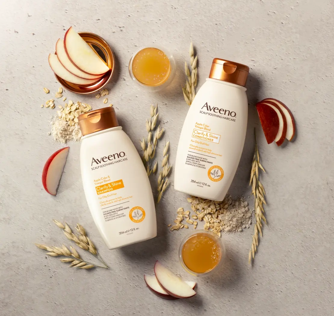 Set of Aveeno® Clarity & Shine Shampoo and Conditioner surrounded by nourishing hair ingredients