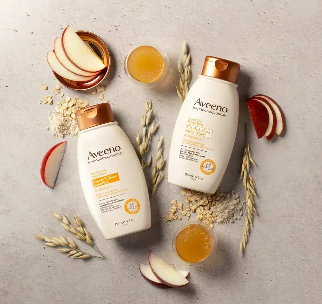 Set of Aveeno® Clarity & Shine Shampoo and Conditioner surrounded by nourishing hair ingredients