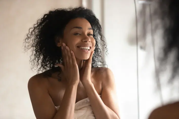 Smiling woman examines face in the mirror
