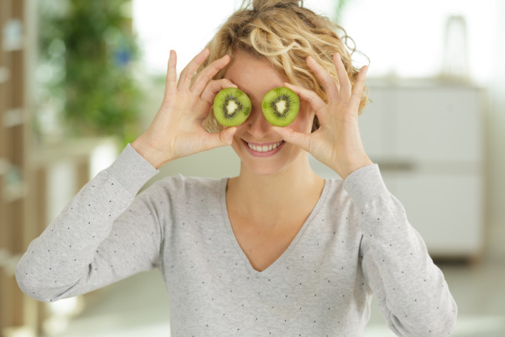 woman with kiwi slices in front of her eyes