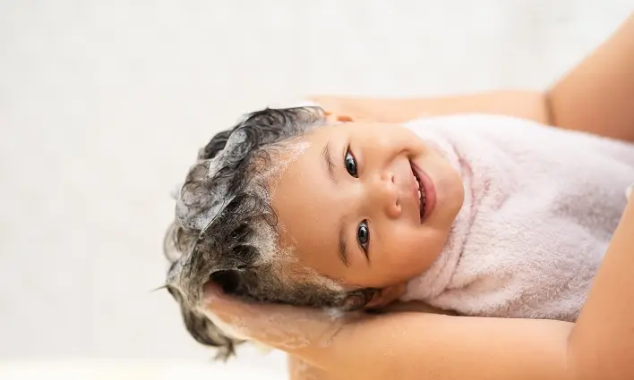 A baby is being carefully hair washed with a towel, highlighting a are moment during their bath