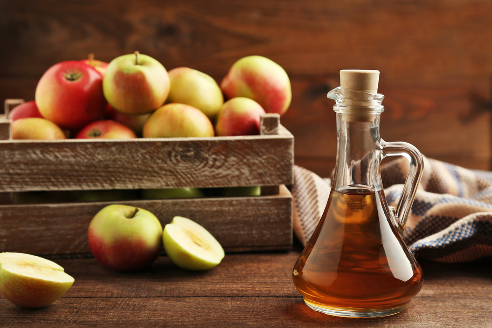 Jug of apple cider vinegar with red apple slices on a wooden table