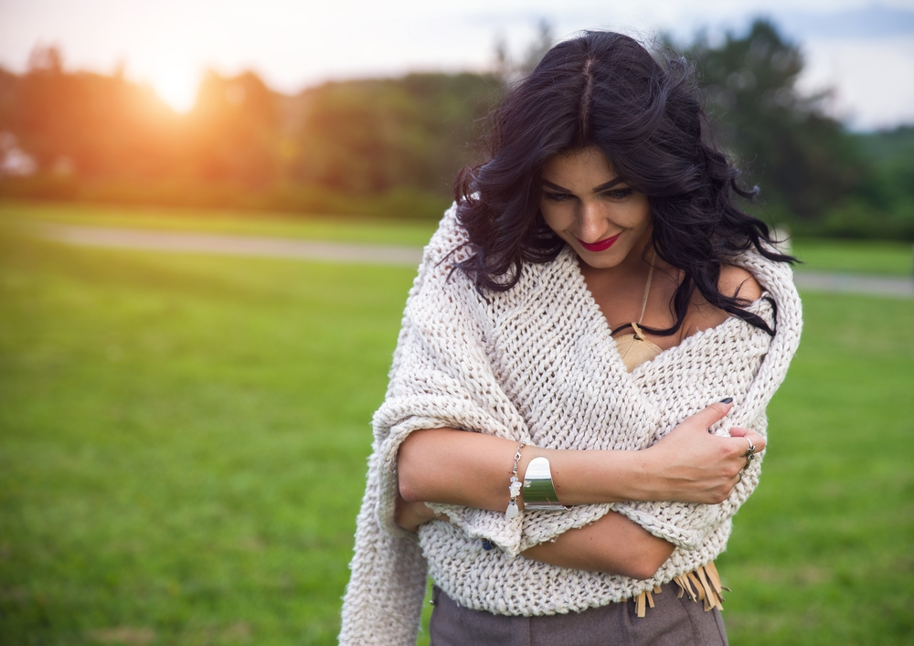 A woman standing in a field wraps her arms around herself.