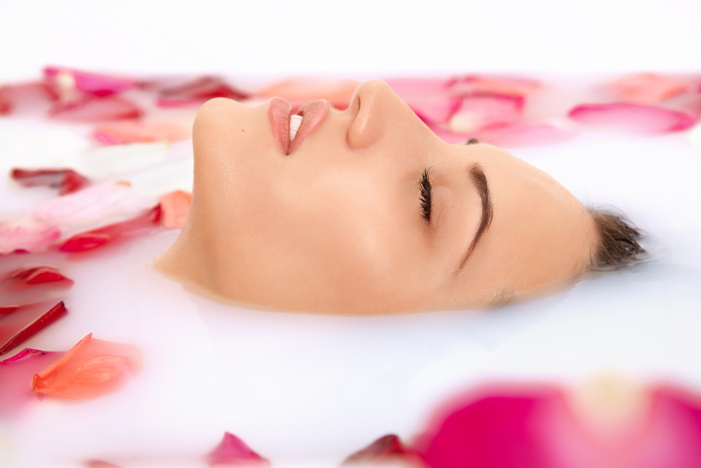 A woman soaks in one of many types of milk baths among floating flower petals.