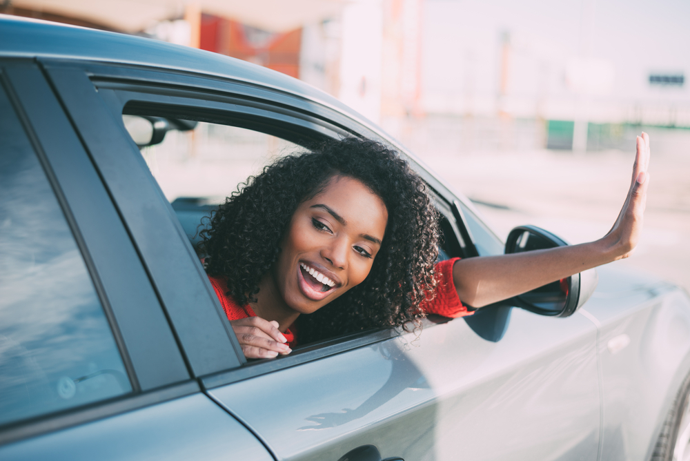 A young adult traveler waves out of a car window.