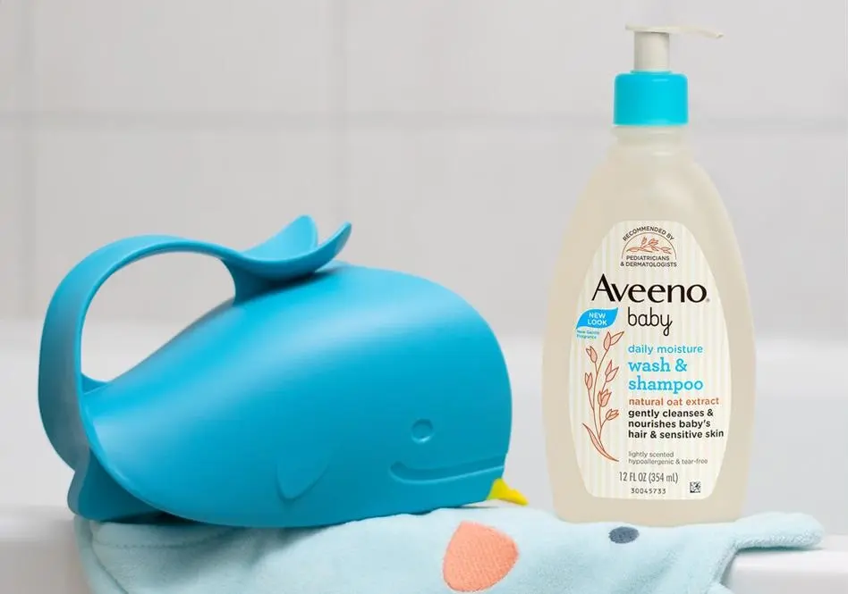 Aveeno® Baby Wash & Shampoo and a whale toy placed on a baby towel sitting on the edge of a bathtub