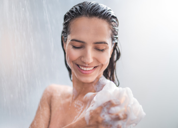 Portrait of happy girl taking shower with gel. She washing with puff