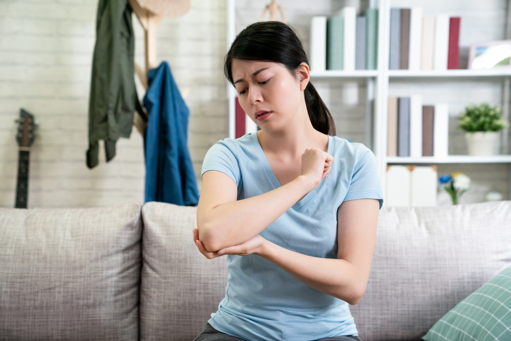 An Asian woman applies a body skincare cream to her dry elbows.