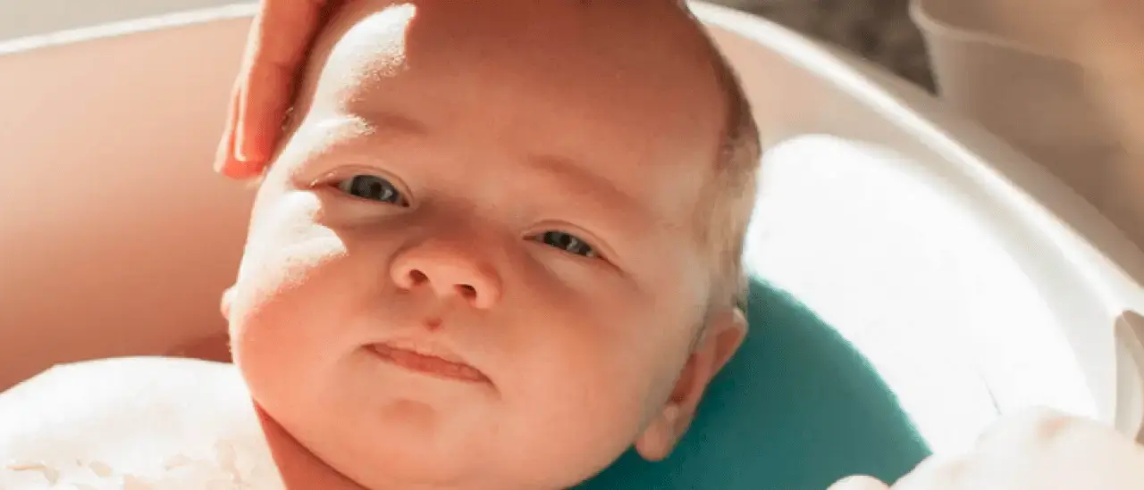 A slightly smiling baby being gently bathed in a baby bath tub
