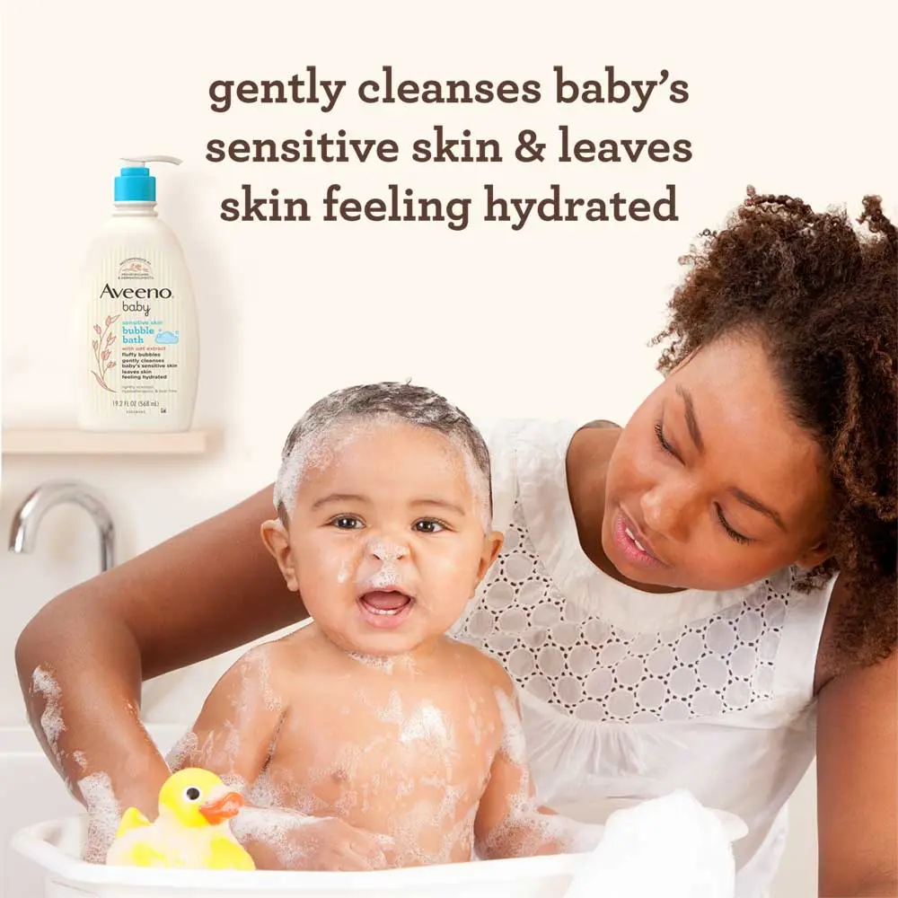 Woman bathing baby in a small bathtub with Aveeno® Baby Bubble Bath bottle in the background.