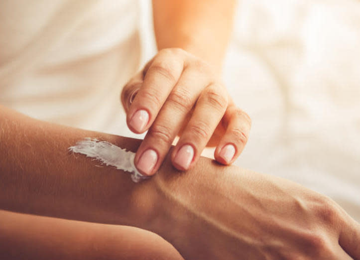 Cropped image of beautiful young woman applying hand cream while sitting on bed at home