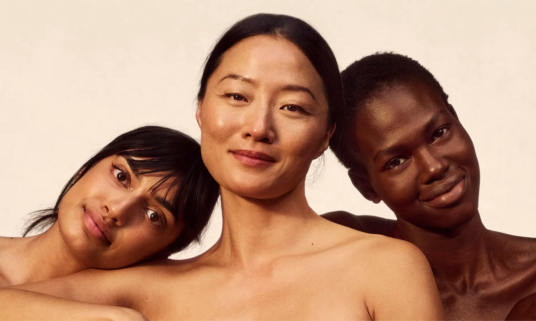 Three women faces smile at the camera, showcasing their natural beauty and skin health.