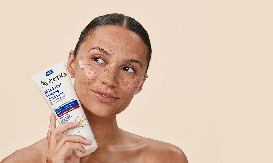 Woman with freckles holds a tube of Aveeno Skin Relief Ointment, showcasing the product application