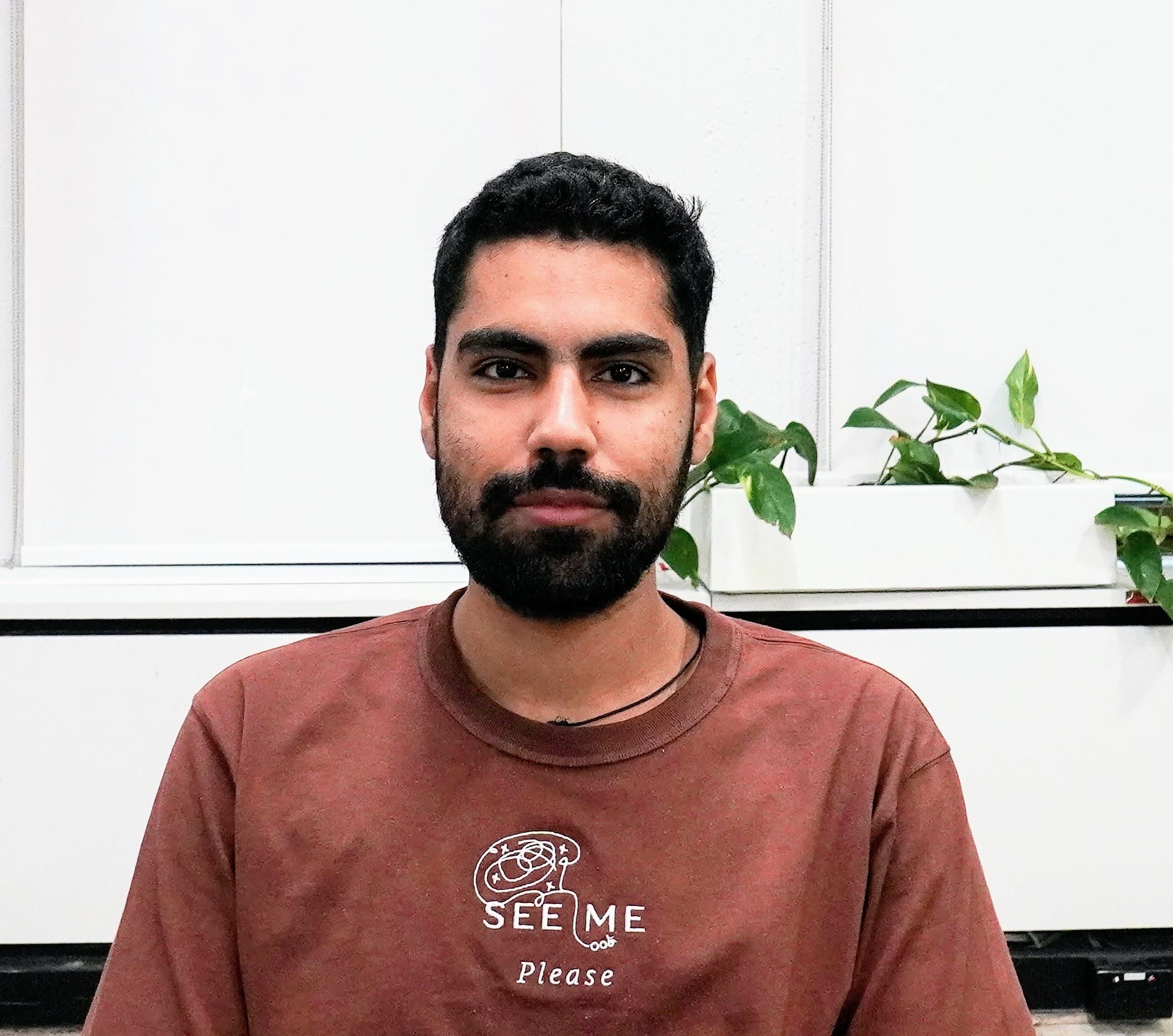 Photo of Bhavya, he's smiling, has plenty of facial hair like any good engineer and is wearing a See Me Please branded brown tee 