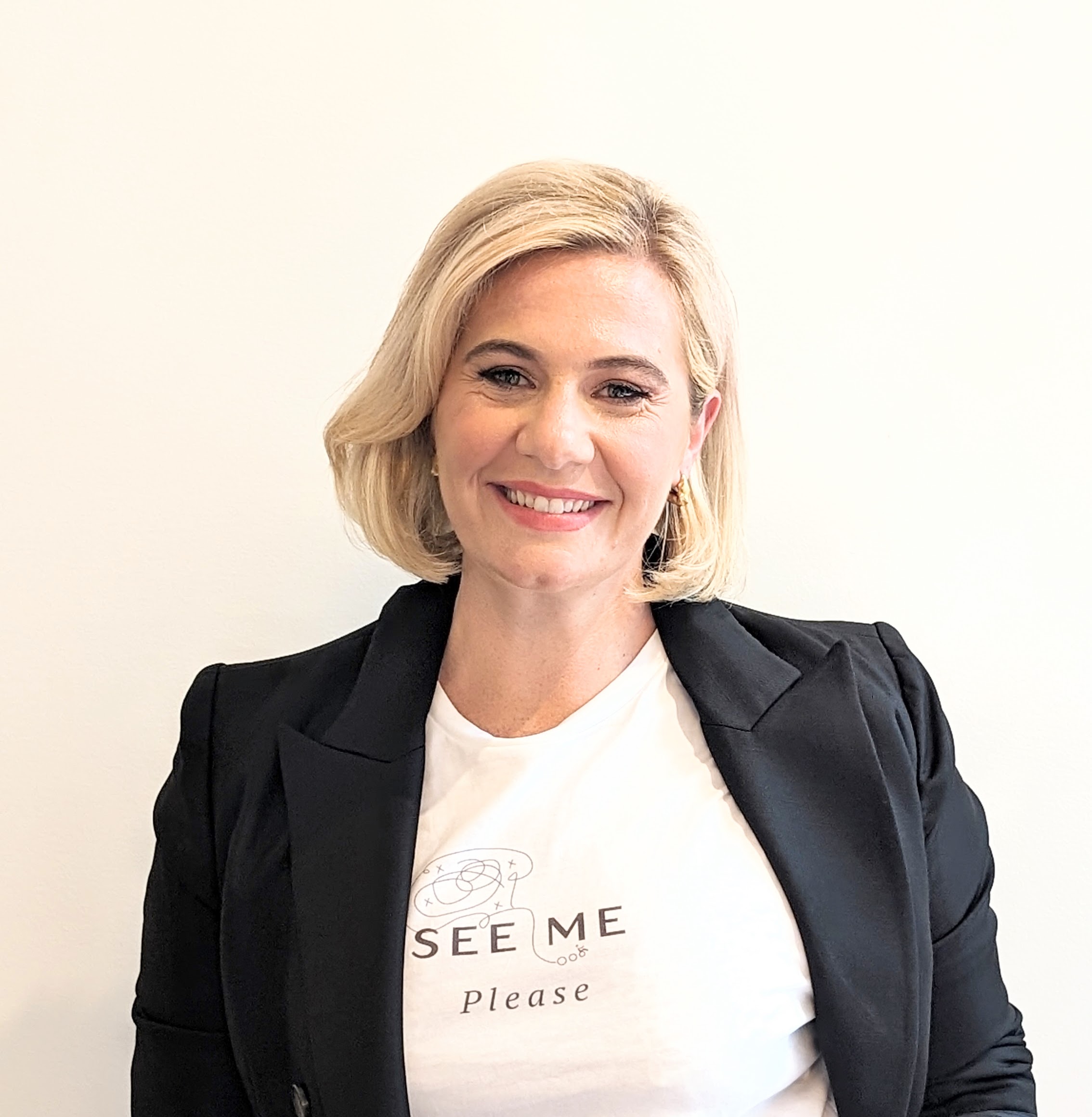 Headshot of Katie. She's got blonde short hair and sporting a See Me Please t-shirt. She looks fresh and relaxed, the photo must have been prior to startup life