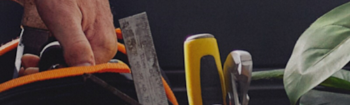 Close-up of a handyman carrying a tool kit with hammer, ruler, level, screwdrivers and other tools, with a green leafy plant in the background