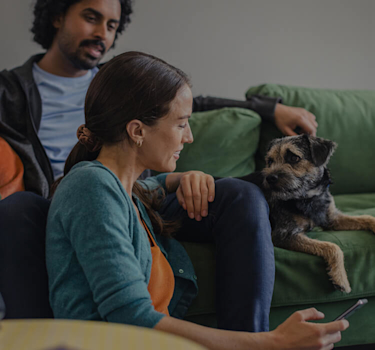 Young dad looking at his smartphone while holding a small baby in his arms with a bright ceiling light and stripy wallpaper in the background