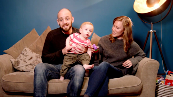 Family with toddler sitting on a brown sofa with a large round floor lamp behind them