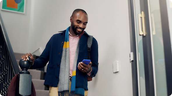 Smiling man wearing a navy jacket and brightly coloured scarf walking down the stairs while looking at a smartphone with a black framed door at the bottom of the stairs on the right