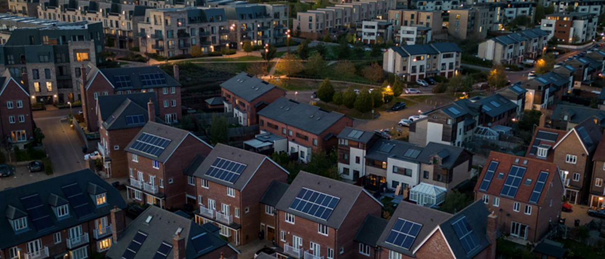 Aerial view of primarily brick-built housing development at dusk. Some of the houses have lights on and most have solar panels on the roof.
