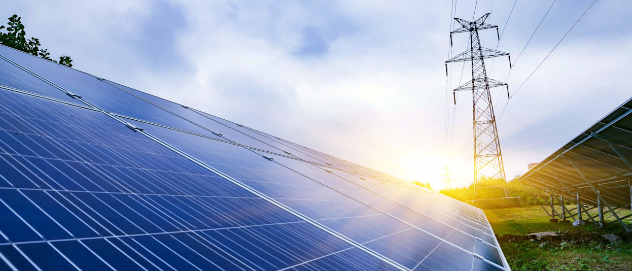 Close-up of large solar panels in a field with an electricity pylon in the background