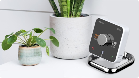 Hive Thermostat sitting on a white unit next to a large concrete plant pot and a smaller ceramic plant pot with a leafy green plant inside it