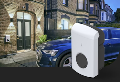 Dark blue car sitting in driveway in front of a brown brick house with a charging cable attached to the car from a unit on the wall, with a Hive EV Charger superimposed in the bottom right corner