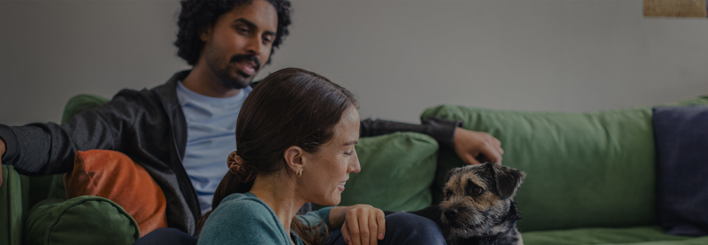 Young dad looking at his smartphone while holding a small baby in his arms with a bright ceiling light and stripy wallpaper in the background