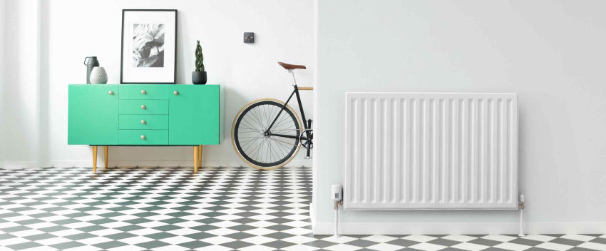 Large hallway with black and white floor tiles, a radiator in the foreground wall with a Hive Radiator Valve attached, a green drawer unit in the background next to a Hive Thermostat on the wall and a bike propped up against the wall