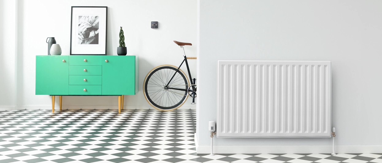 Large hallway with black and white floor tiles, a radiator in the foreground wall with a Hive Radiator Valve attached, a green drawer unit in the background next to a Hive Thermostat on the wall and a bike propped up against the wall
