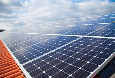 Close-up of solar panels on a red-tiled roof with a cloudy blue sky in the background