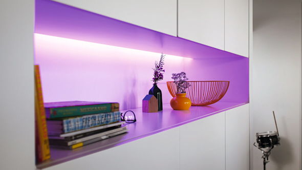 Floor to ceiling white cabinets with a shelf in the middle that has a strip of bright purple light at the back with pots, baskets and books sitting on the shelf