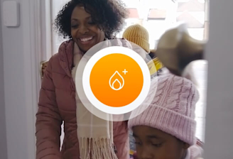 Mother and daughter dressed in winter clothes and walking into their home with an orange icon superimposed in the middle of the image