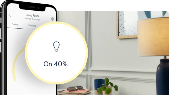 Side angle of smartphone showing the Hive app with a pop-out icon on the left of the image showing the Hive bulb dimmer set-up, with table lamp in a hallway in the background image